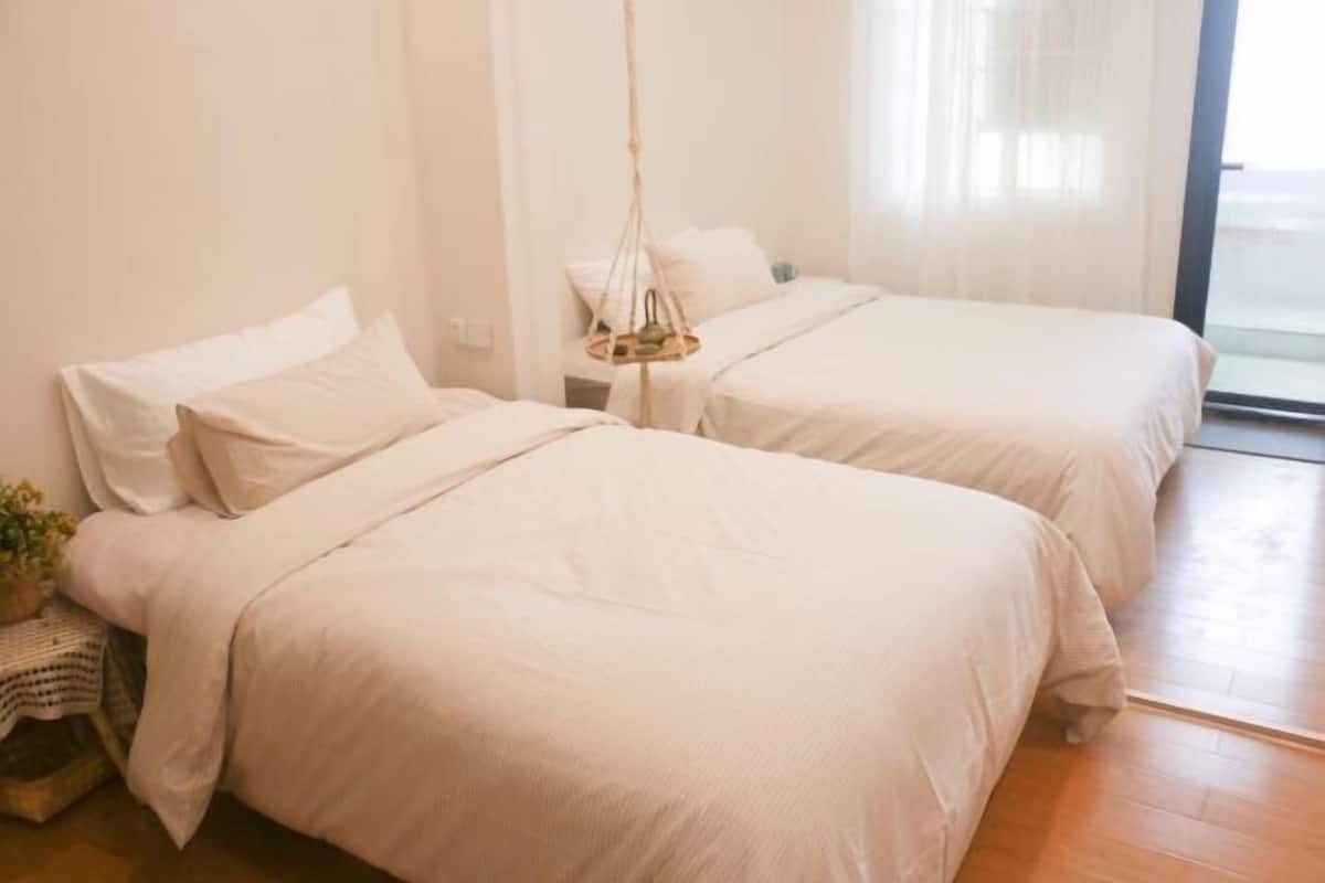 A bedroom with two beds, a hanging light fixture, and a window with sheer curtains.