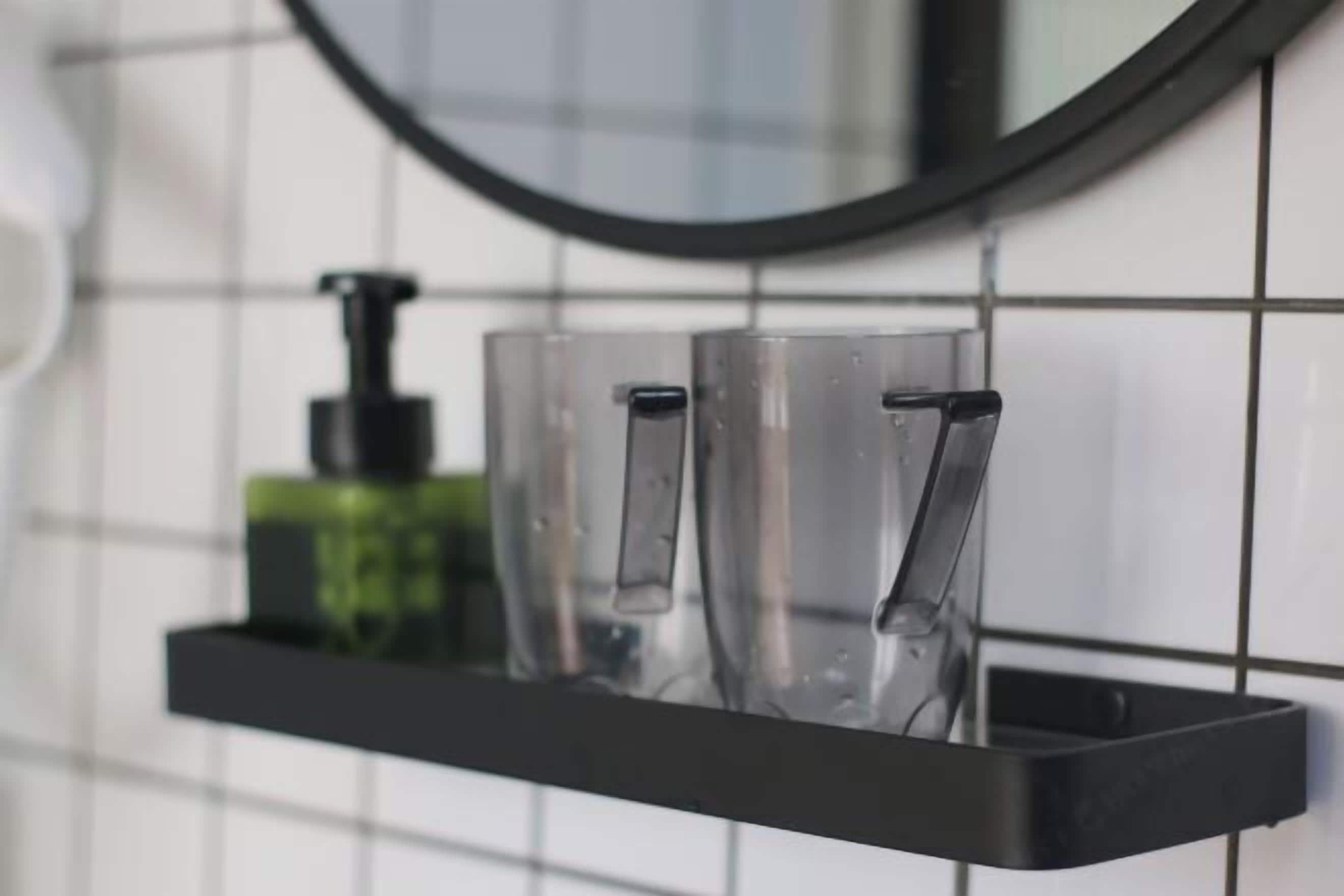 A bathroom with a black shelf holding clear glasses and a green bottle.