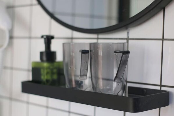 A bathroom with a black shelf holding clear glasses and a green bottle. - Qianzihu Boutique Guesthouse (Fuzhou)