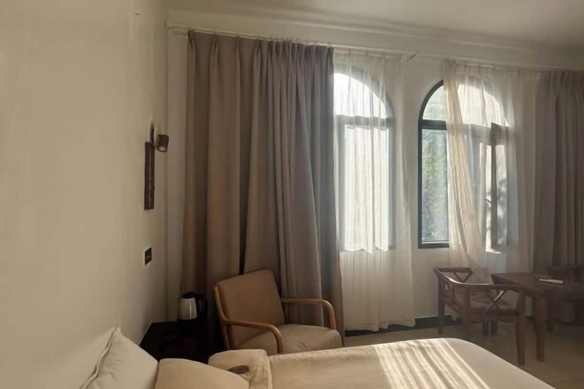 A hotel room with a bed, two chairs, a table, and large windows with curtains.