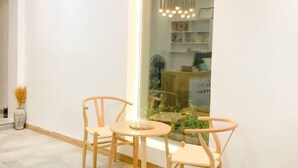 A room with a round wooden table and two chairs, a vase with dried plants, and a view of a garden through a glass wall.