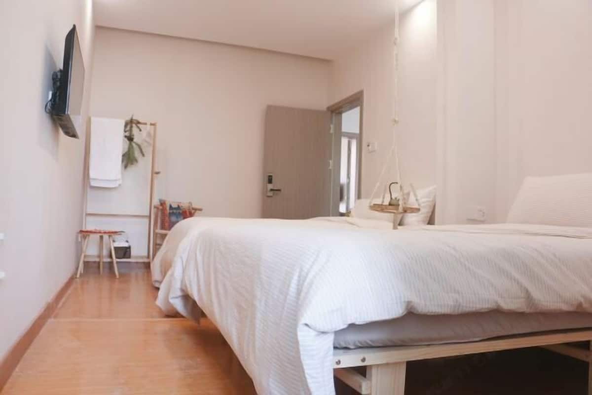 A bedroom with a large bed, a TV mounted on the wall, and a small desk with a chair.