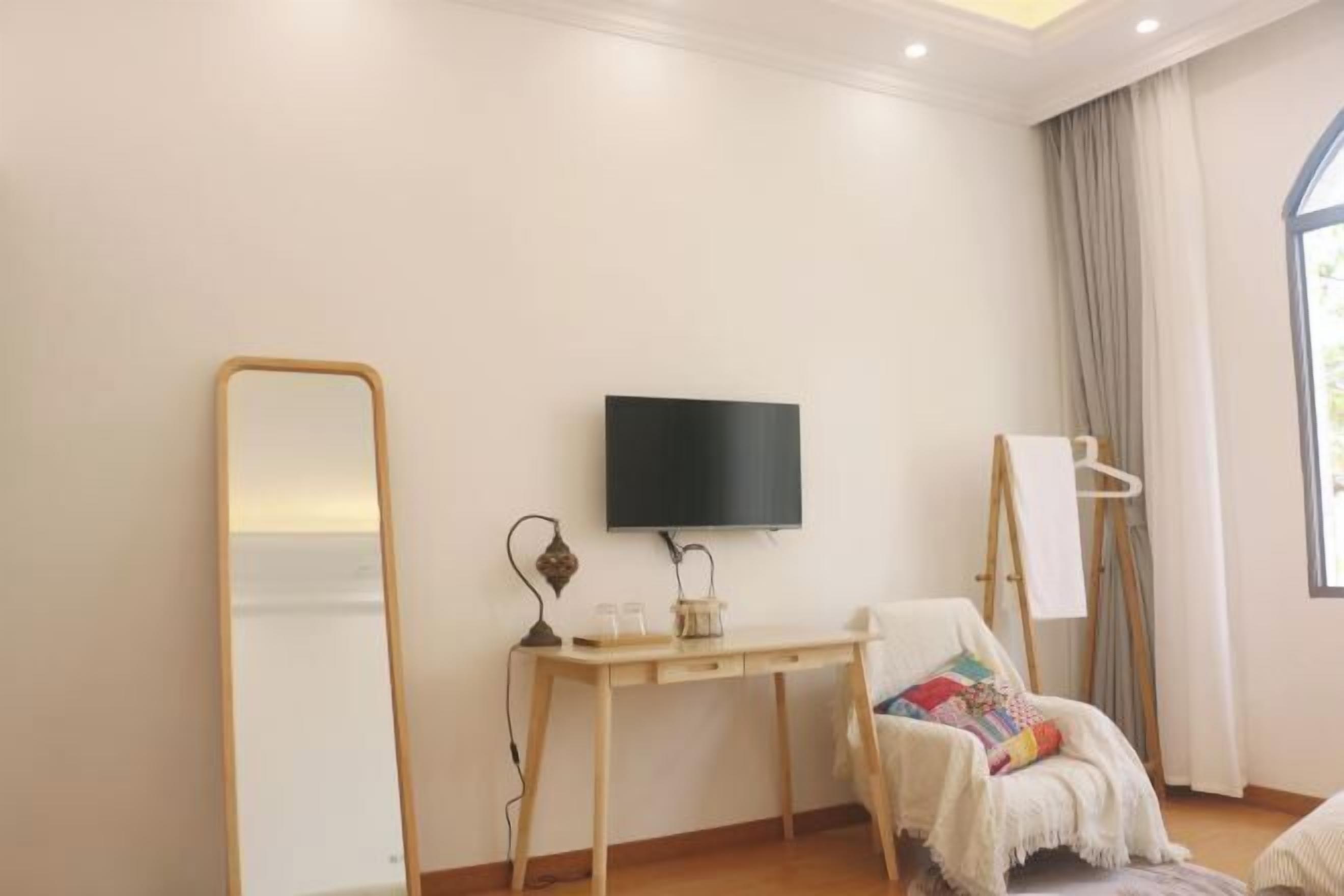 A room with a wooden desk, a flat-screen TV, a large mirror, and a chair with a colorful cushion.