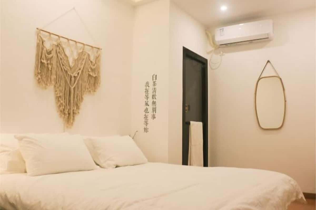A bedroom with a bed, a wall-mounted air conditioner, a door, and a wall decoration.