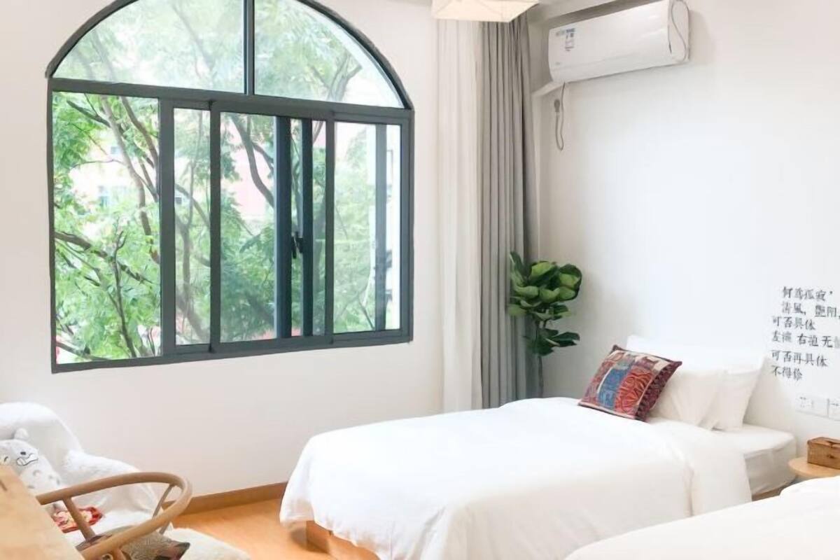 A bedroom with a large arched window, a bed, a chair, and a wall-mounted air conditioner.