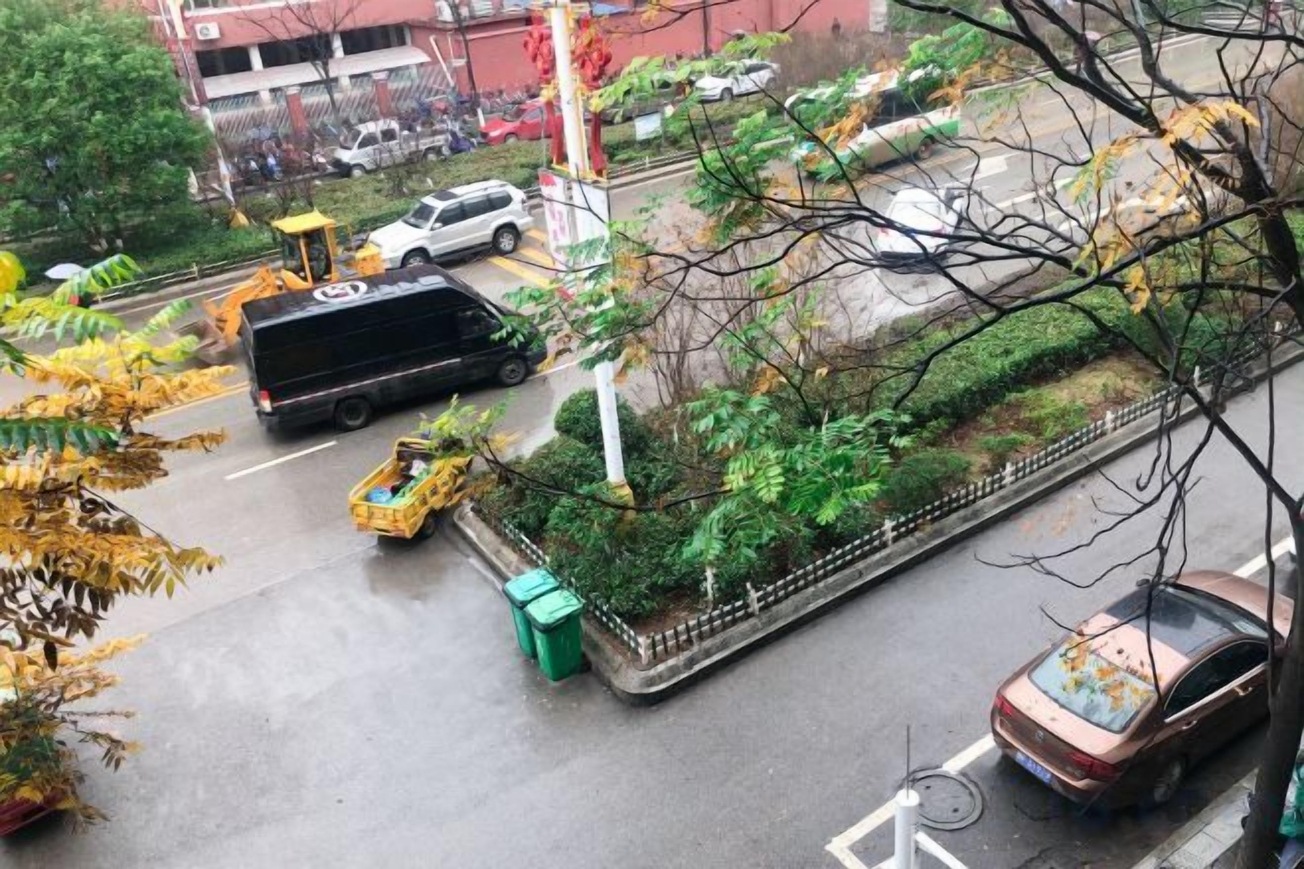 A street scene with vehicles, a bicycle, and a green trash bin.