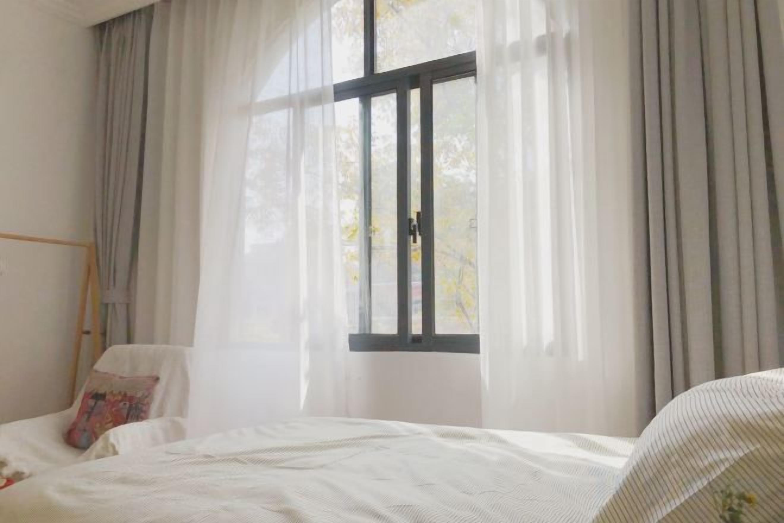 Un dormitorio con cama, ventana con cortinas y mesita de noche.