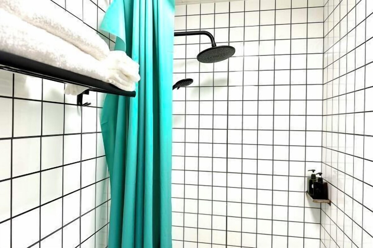 A bathroom with white tiled walls, a black showerhead, and a teal shower curtain.