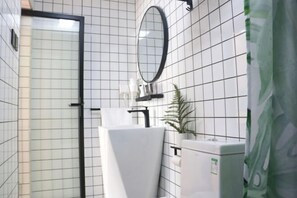 A bathroom with white tiled walls, a mirror, a sink, a towel, and a plant. - Qianzihu Boutique Guesthouse (Fuzhou)