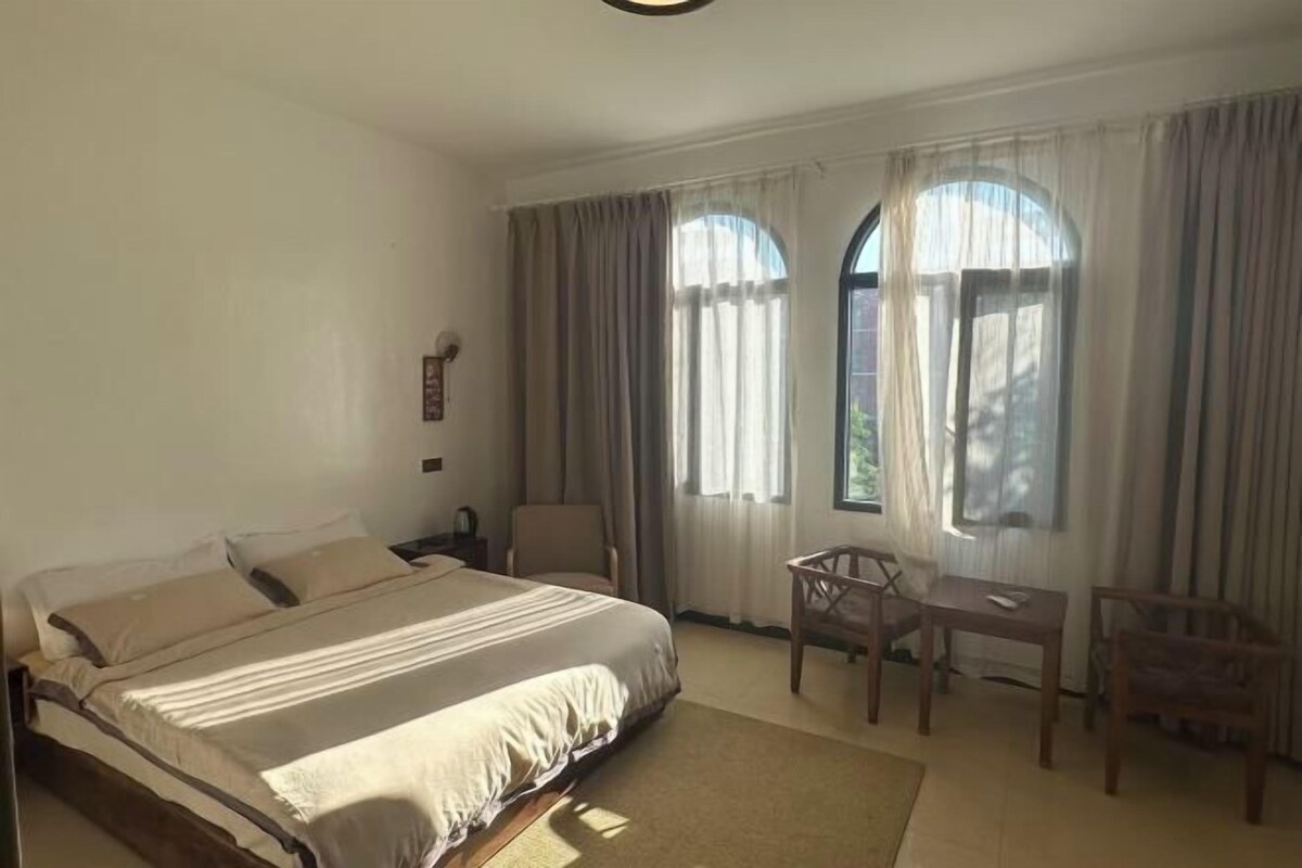 A bedroom with a bed, two chairs, a small table, and a window with curtains.
