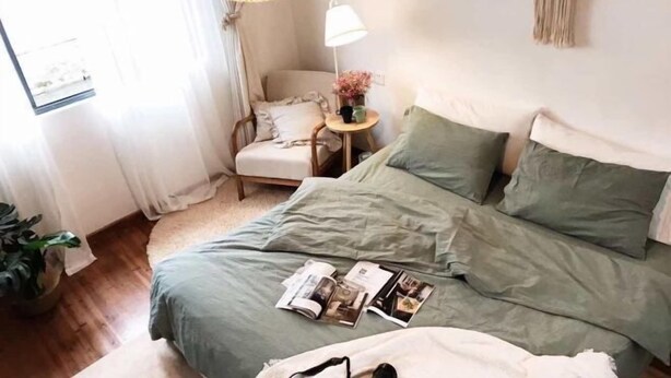 A bedroom with a bed, a chair, a lamp, and a small table with a plant.