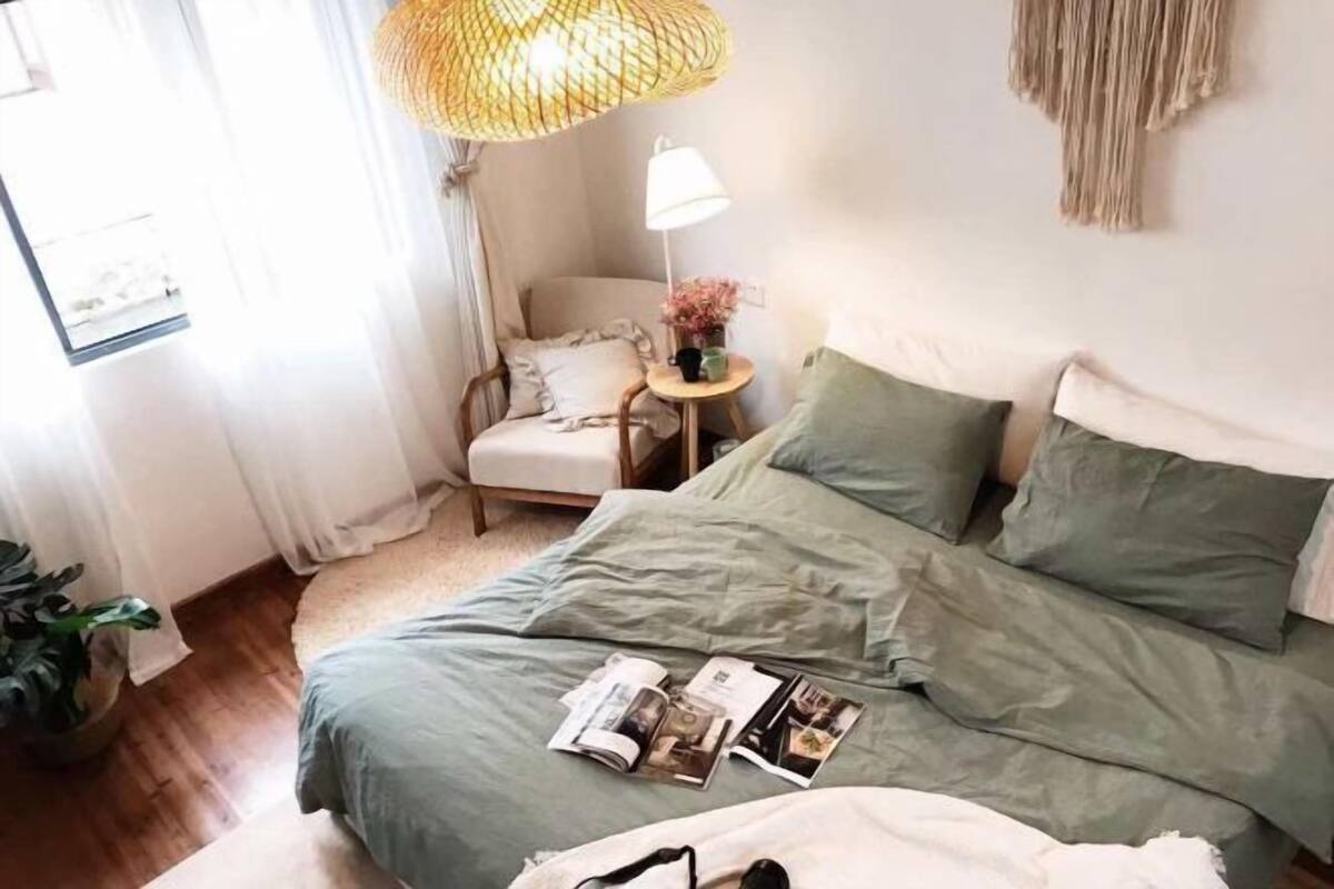 A bedroom with a bed, a chair, a lamp, and a small table with a plant.