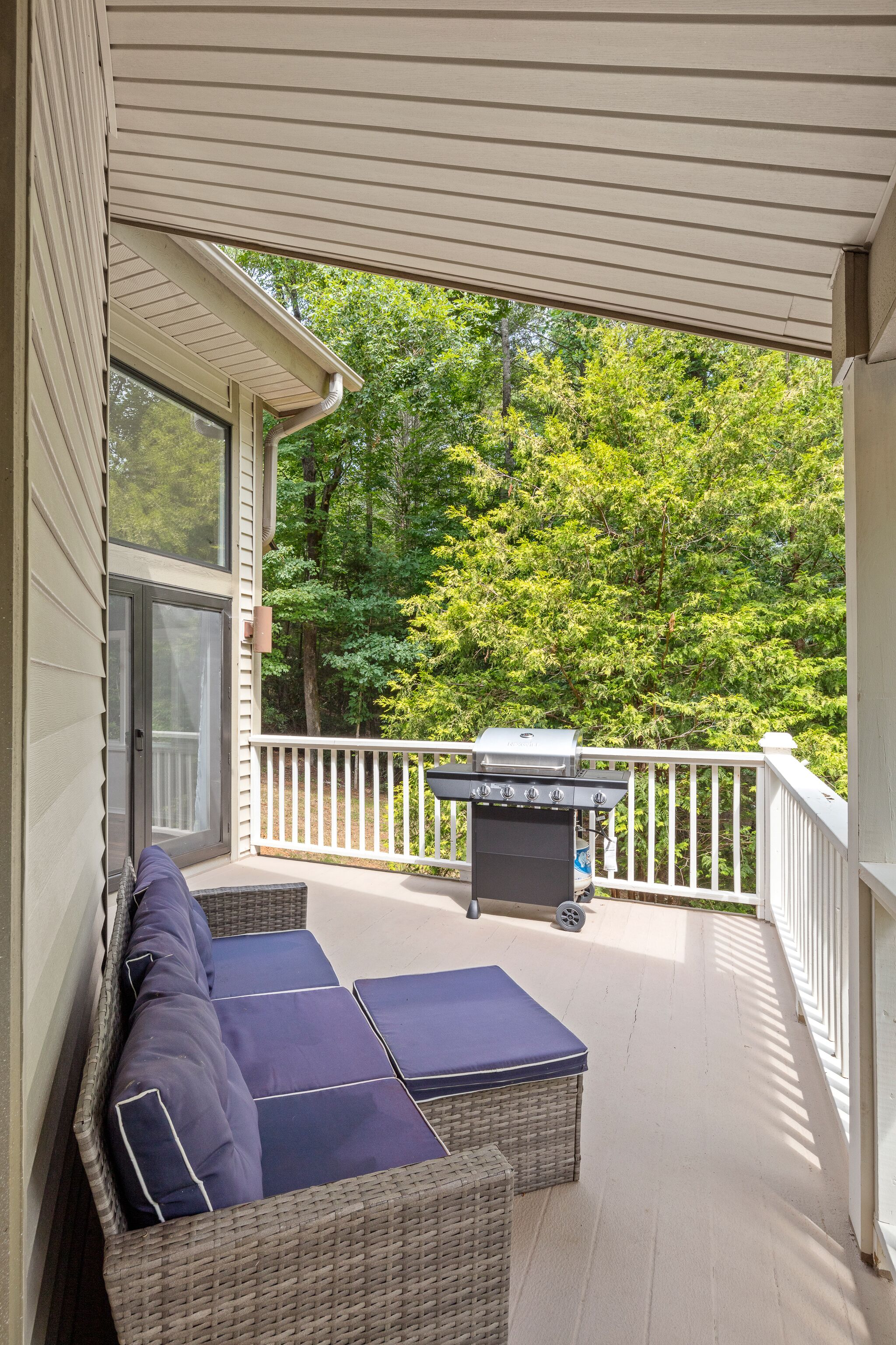 A covered porch with wicker furniture and a grill.