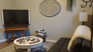 Una sala de estar con televisor, un cráneo decorativo, un espejo redondo, un sofá y una lámpara.