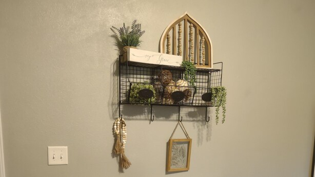 Un comedor con una mesa de madera, dos taburetes, un estante en la pared con plantas, un cuadro enmarcado y un cuenco sobre la mesa.