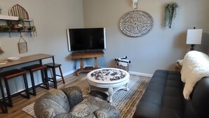 Una sala de estar con ventilador de techo, televisor, una mesa redonda de centro, sofá y un adorno en la pared.