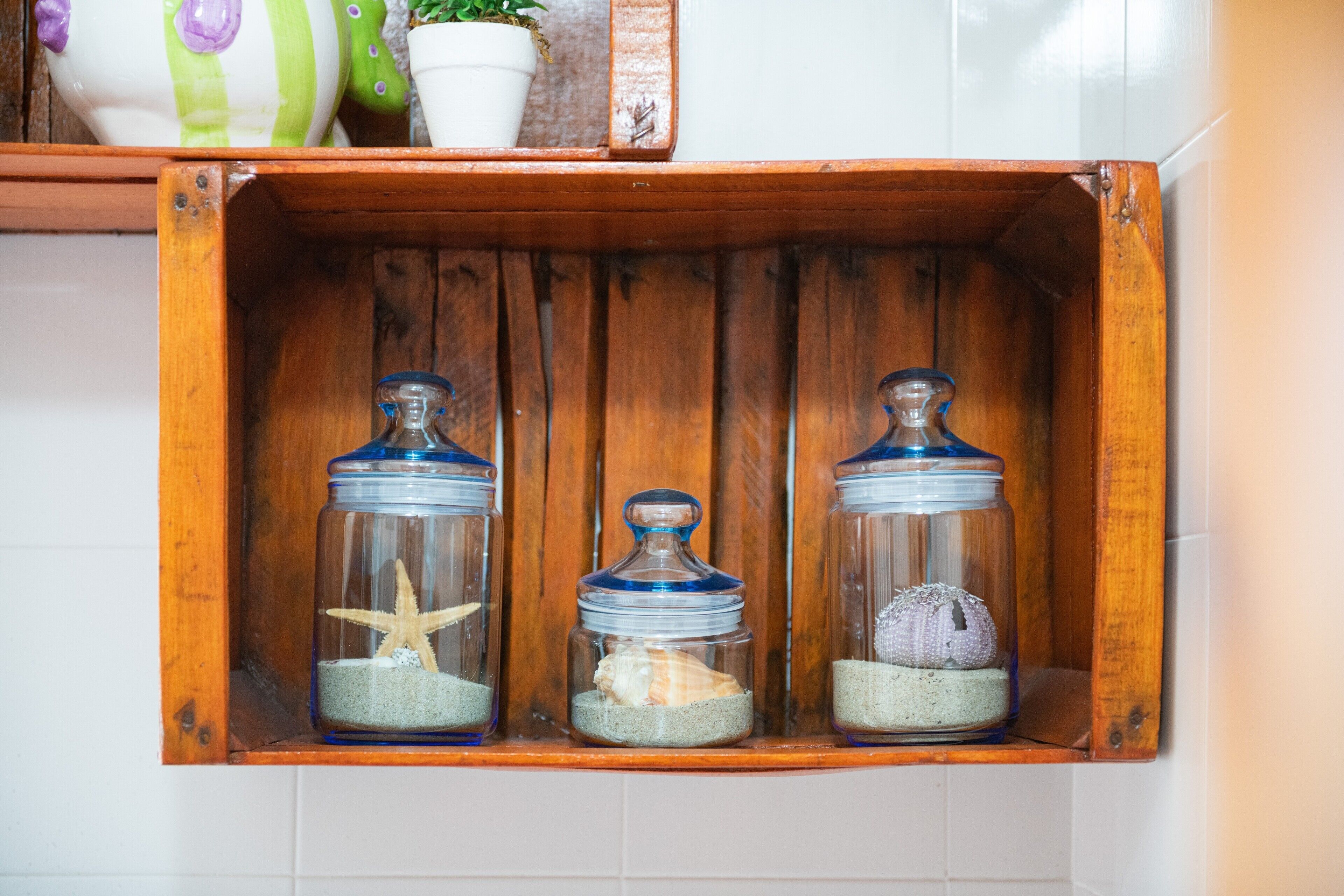 A wooden shelf with three glass jars containing seashells and a starfish.