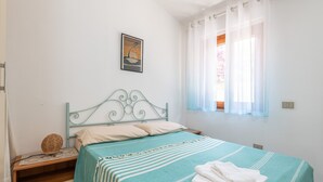 Une chambre à coucher avec un lit, une table de chevet, un tableau accroché au mur et une fenêtre avec des rideaux.