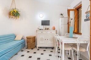 Habitació amb sofà, taula de dinar amb cadires, armari, televisió i planta penjollant.