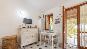 Une pièce comprenant une table à manger, des chaises, un téléviseur, un meuble, un panier en osier et une porte-fenêtre coulissante donnant sur un espace extérieur.
