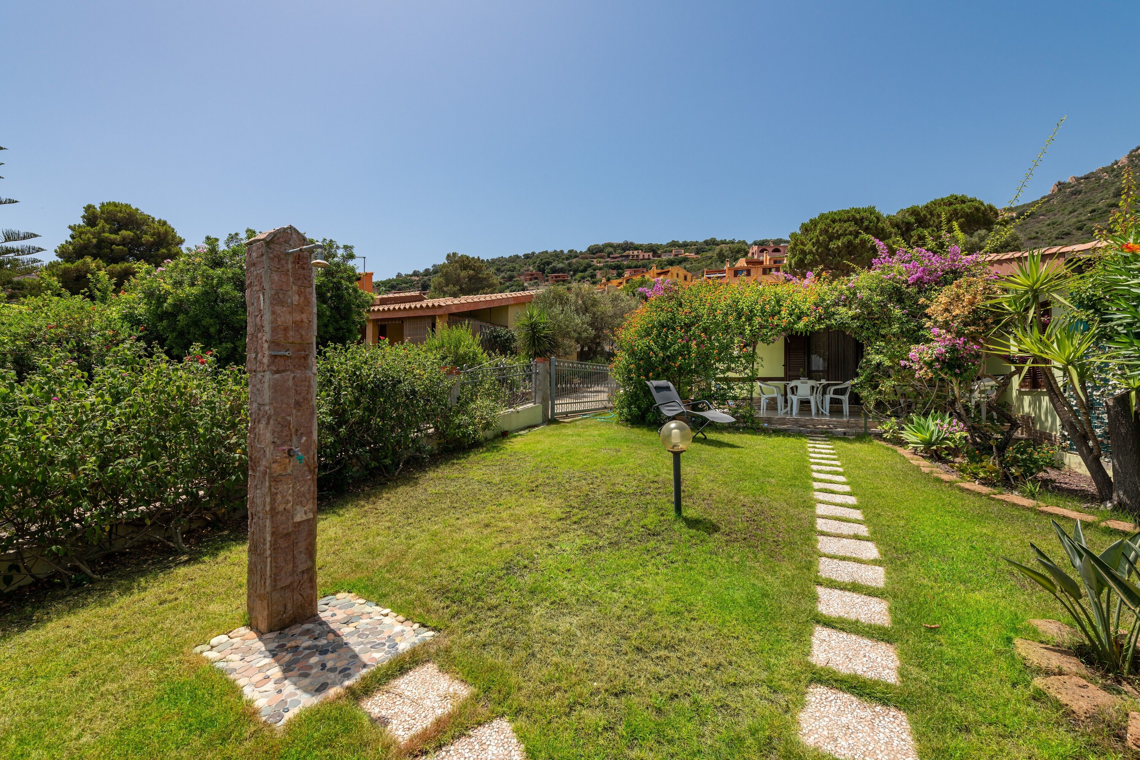 A garden with a stone pillar, a paved path, and a small seating area with a table and chairs.