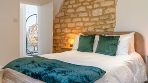 A bedroom with a stone wall, a bed with white and green bedding, and a nightstand with a lamp. - Landers, Cheltenham - sleeps 10 guests  in 5 bedrooms (Cheltenham)