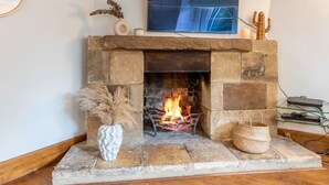 A stone fireplace with a fire, a TV mounted above it, and a cactus decoration on the mantel. - Landers, Cheltenham - sleeps 10 guests  in 5 bedrooms (Cheltenham)