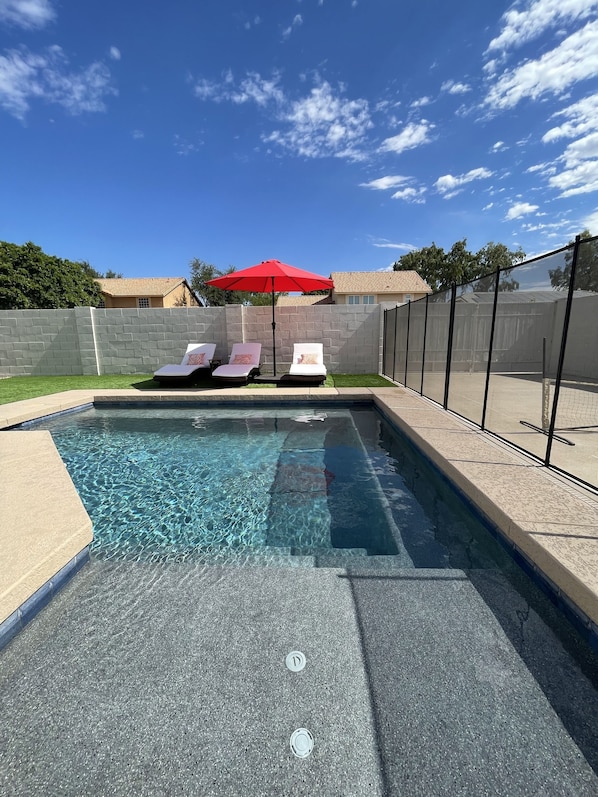 Relax by the pool surrounded by a deck and a brick wall.