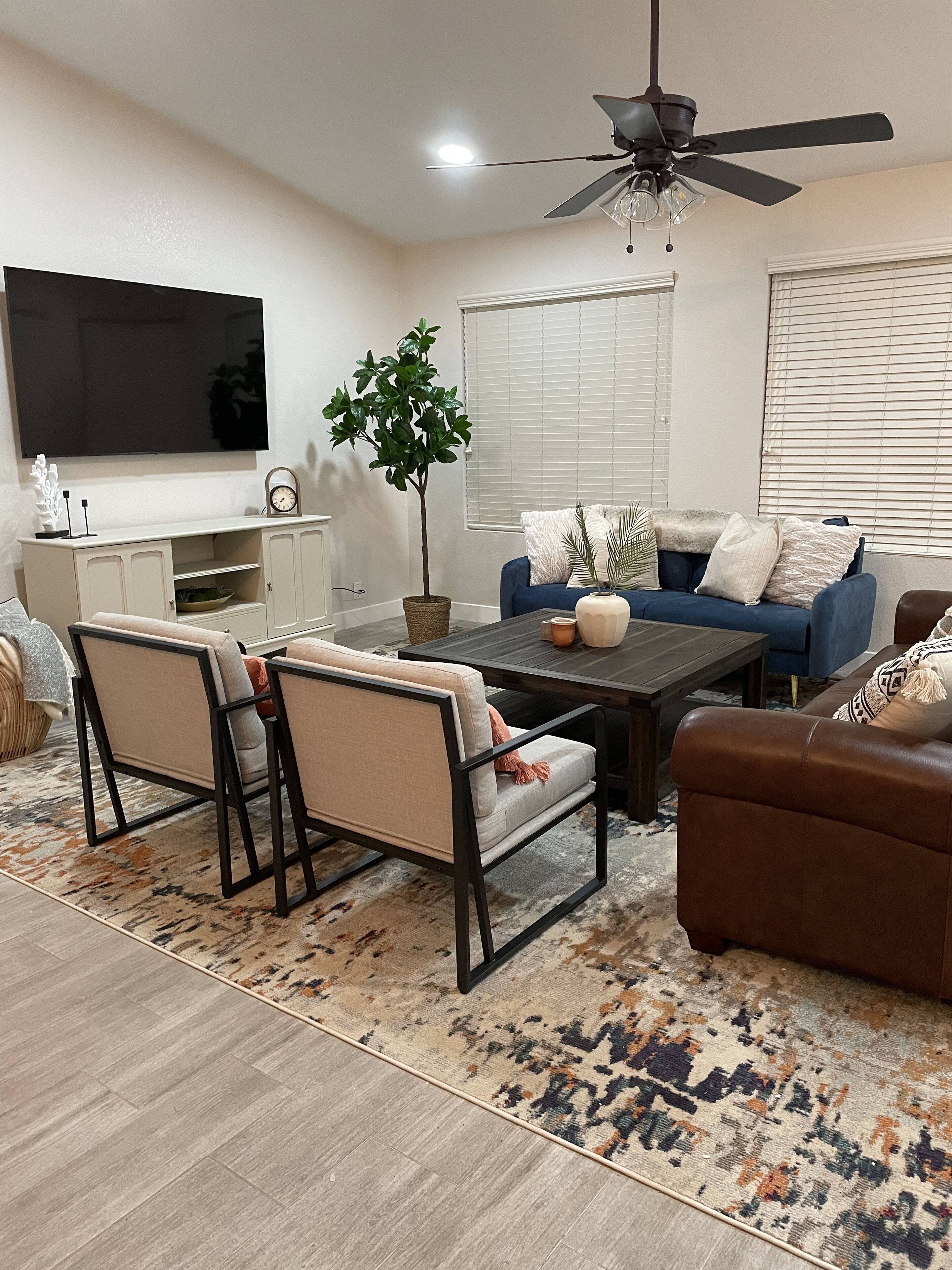 A modern living room with a flat-screen TV, a ceiling fan, a dining table, and two sofas.