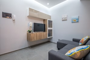 A modern living room with a flat-screen TV, grey sofa, and decorative pillows.
