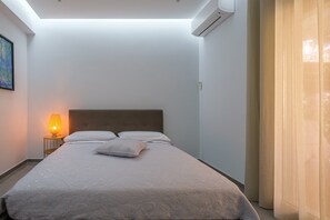 Ein Schlafzimmer mit einem Bett, einem Nachttisch mit Lampe, einer Klimaanlage und einem Bild an der Wand.