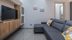 Una sala de estar moderna con un televisor de pantalla plana, un sofá gris y dos cuadros colgados en la pared.