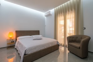 A bedroom with a bed, bedside lamp, chair, and curtains.