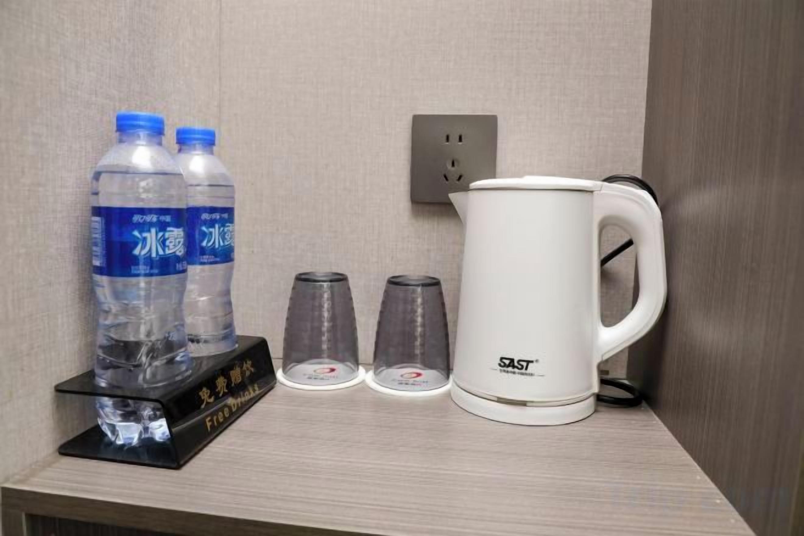 A hotel room with a minibar containing two water bottles, two glasses, and a white coffee maker.