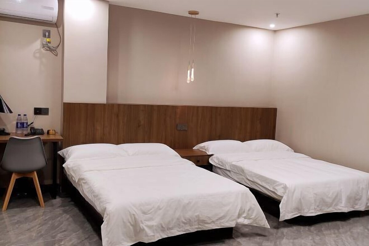 A hotel room with two single beds, a desk with a chair, a wooden headboard, and a hanging light fixture.