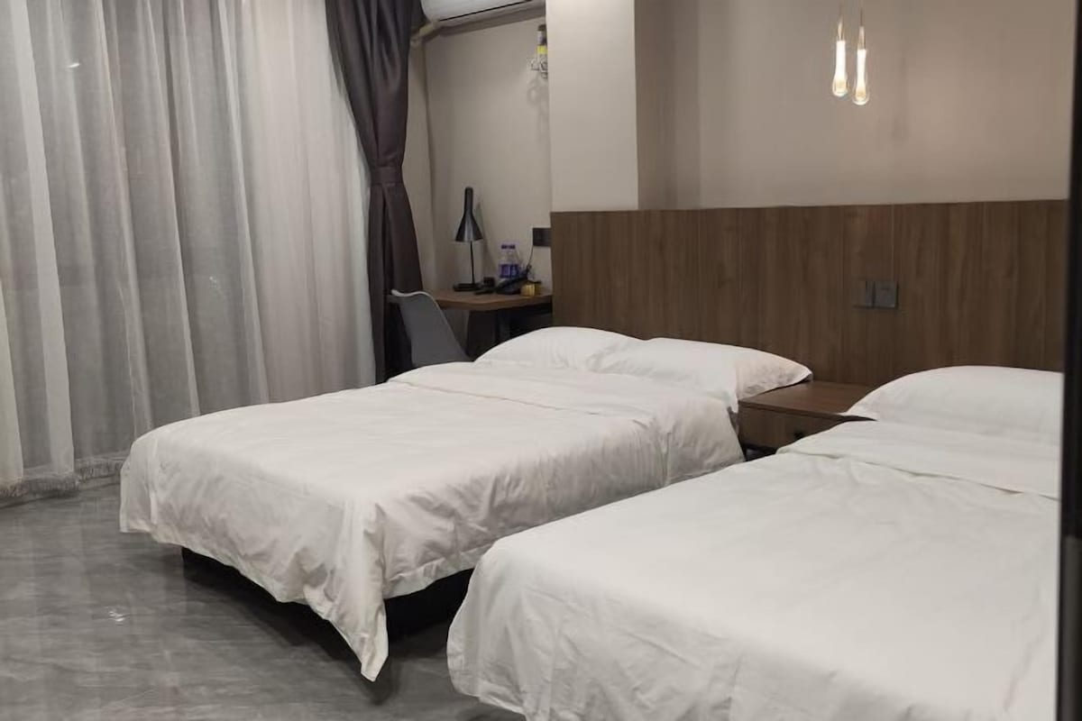 A hotel room with two beds, a desk, a chair, and a lamp.