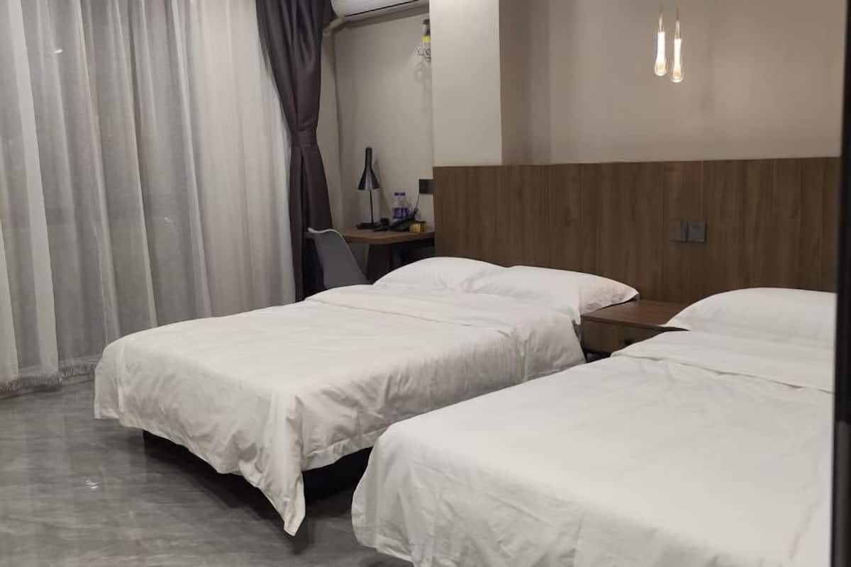 Quarto de hotel com duas camas, uma escrivaninha, uma cadeira e uma luminária.