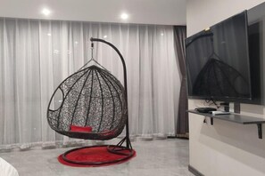 A room with a hanging chair, a flat-screen TV, and a red circular rug. - Dalian Jiayan Collection Hotel (Dalian)