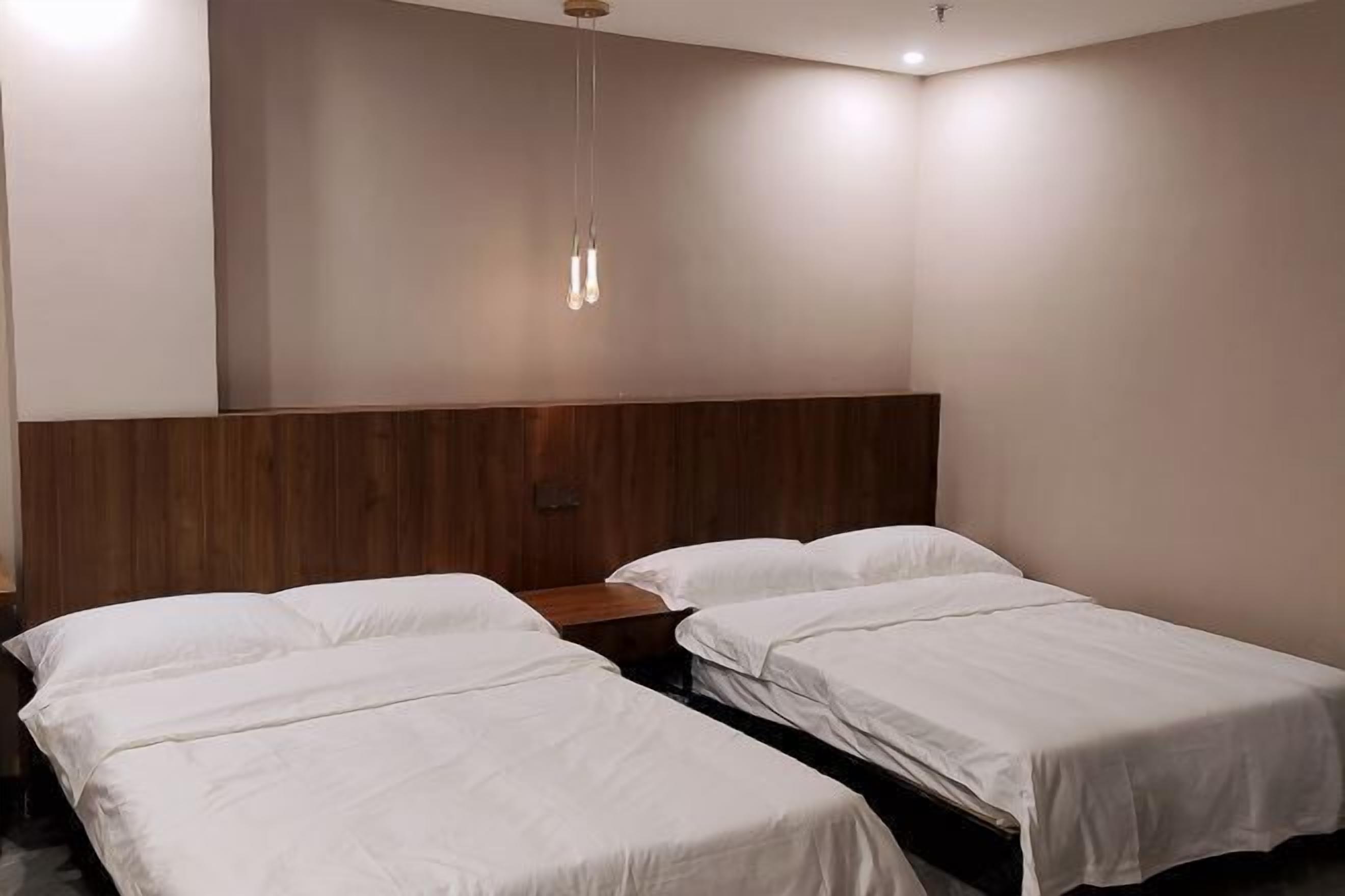 Habitación de hotel con dos camas individuales, un cabecero de madera y una lámpara colgante.