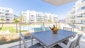 Un balcon avec une table, un panier en osier rempli de fruits et une piscine en arrière-plan.