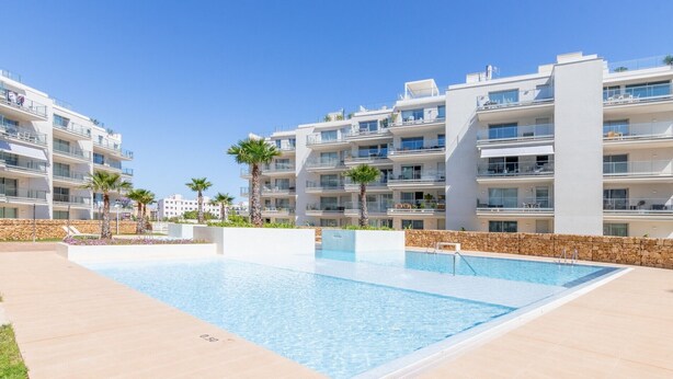 Un immeuble d’appartements moderne doté d’une piscine, de balcons et de palmiers.