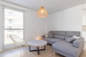 Uma sala de estar moderna com um sofá cinza, uma mesa redonda, uma cadeira de vime e um candeeiro pendente.