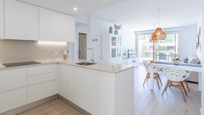 A modern kitchen with white cabinetry, a central island, and a dining area with white chairs.