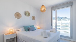 A bedroom with a bed, bedside tables, decorative wall hangings, and a view of buildings through a large window.