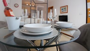 A dining area with a glass table, white plates, wine glasses, and a bottle.