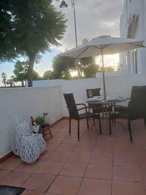 Une terrasse extérieure avec une table et des chaises, un parasol blanc et une plante en pot.