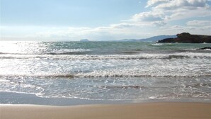 A beach with waves, a clear sky, and distant landforms.