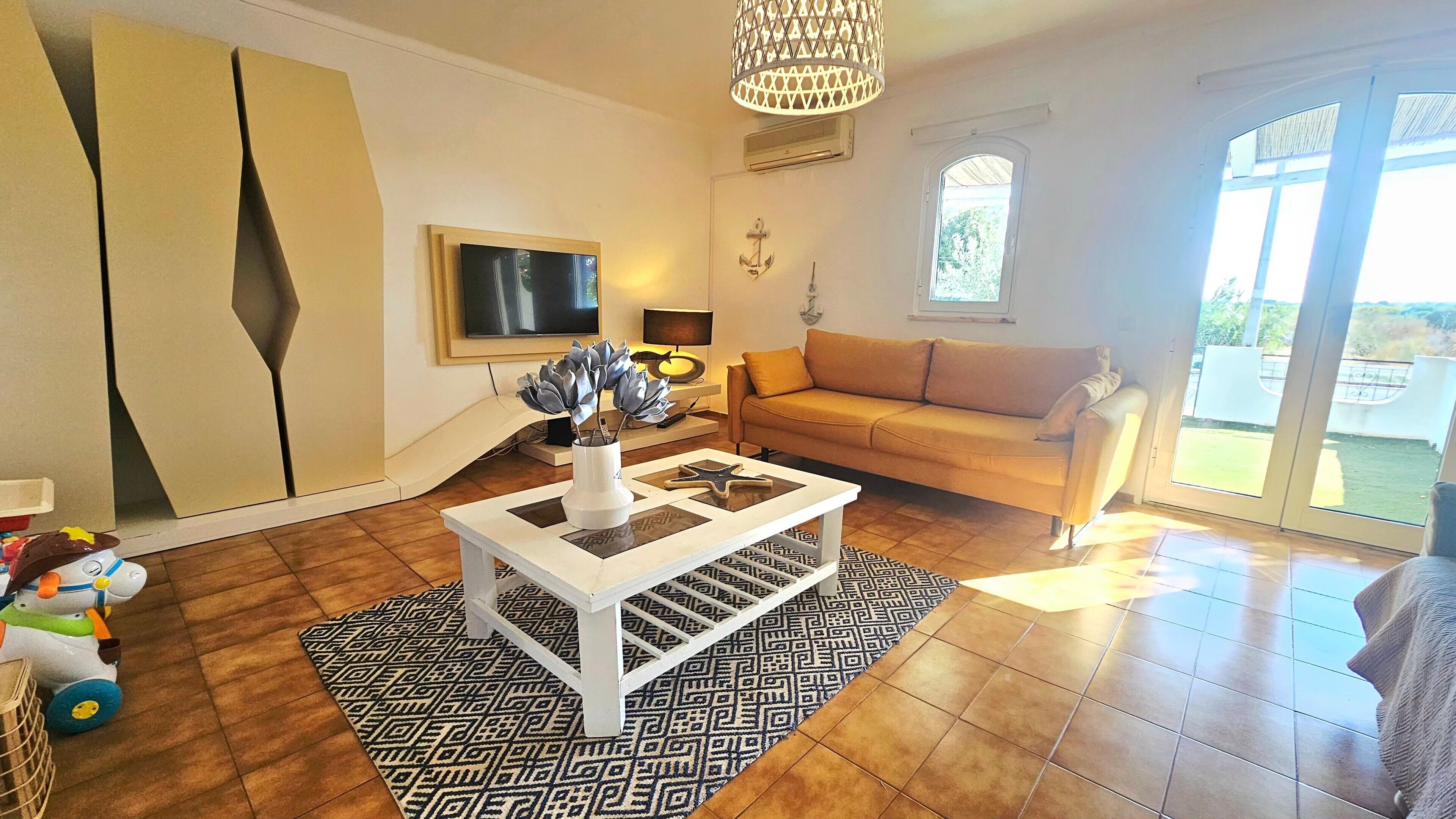 A living room with a sofa, a coffee table, a TV, and a patterned rug.