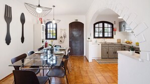 Une cuisine moderne avec des meubles blancs, un coin repas doté d’une table en verre et une porte noire.