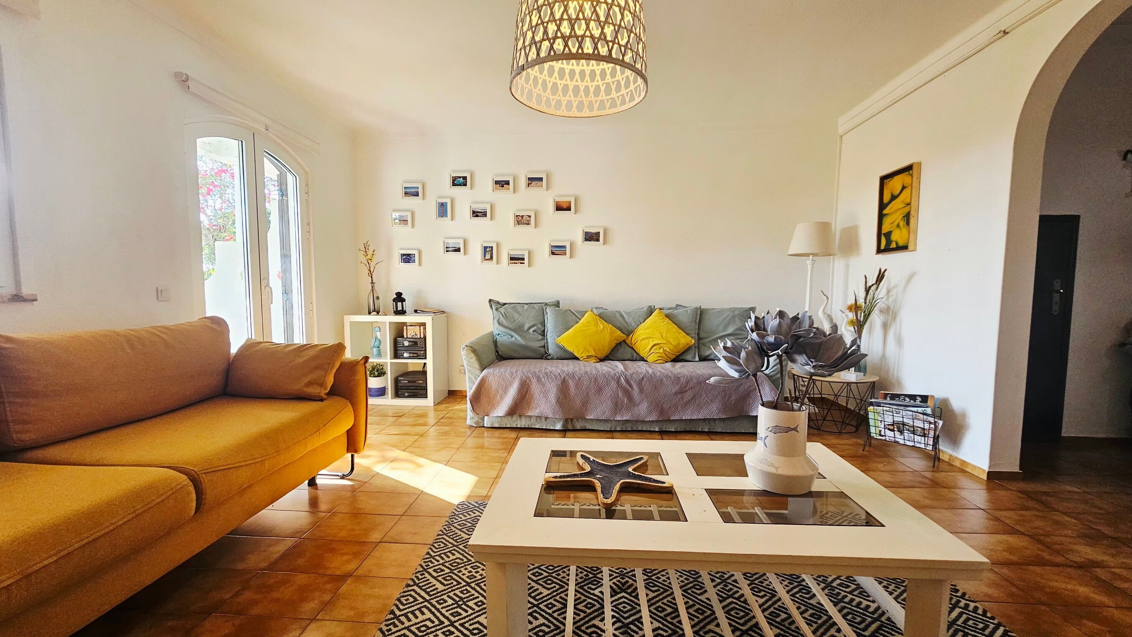 Een woonkamer met een bank, een salontafel, een boekenkast en een wand met ingekaderde foto's.